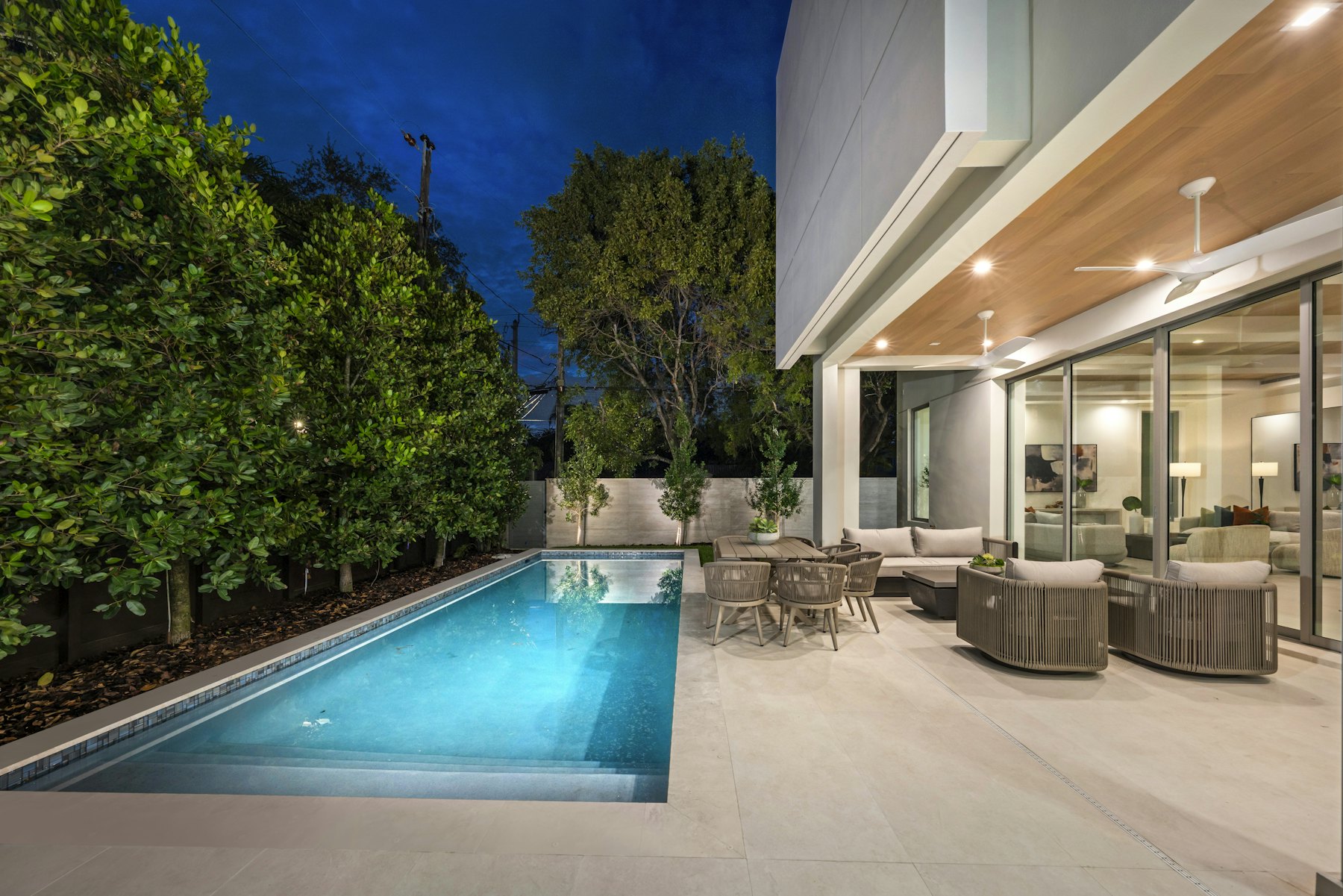 Modern home with a lit swimming pool and outdoor seating at dusk
